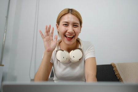 A woman wearing headphones and smiling while waving at the camera