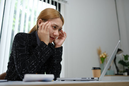 A woman is sitting at a desk with a laptop and a cup of coffee