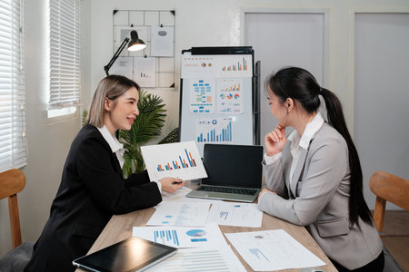 Two women are sitting at a table with papers and a laptopの写真素材
