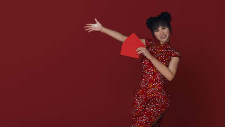 3D Render :beautiful Asian smiling young woman with Chinese traditional dress female cheongsam or qipao holding ang pow or red packet monetary giftの写真素材
