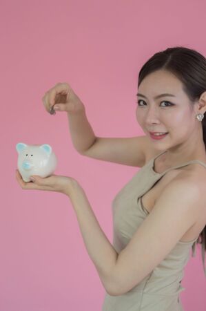 Woman Putting Coin In Piggy Bank on pink backgroundの写真素材