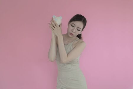 Woman Putting Coin In Piggy Bank on pink backgroundの写真素材