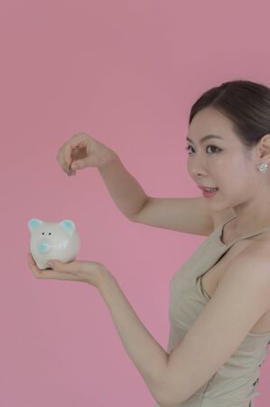 Woman Putting Coin In Piggy Bank on pink backgroundの写真素材