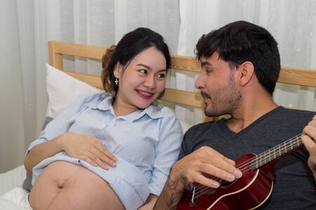 Men playing music for pregnant women in the bedroom.の写真素材