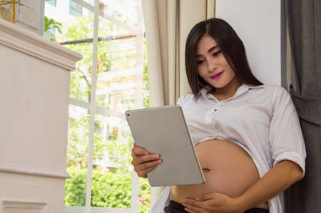 The pregnant woman is playing mobile in the home.の写真素材