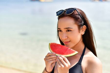Beautiful girl wearing swimsuit eating watermelon beach.の写真素材
