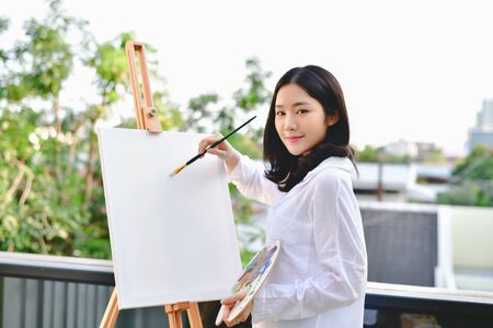 Concept Artist Beautiful girl. Beautiful women are creating art. Beautiful woman is painting happily. Young artist painting outside the house.の写真素材