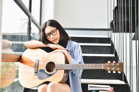 Music Concepts. Asian girls playing guitar. Asian women relaxing with music. Asian women have a happy lifestyle. Beautiful Asian girl playing guitar at home.の写真素材
