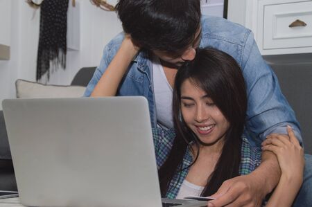Couples Concept. Lovers are playing in the living room. Couples are shopping through the Internet. Lovers are playing a notebook happily. Lovers are relaxing in the living room.の写真素材