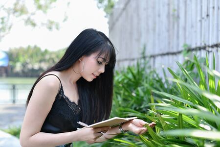 Education Concepts. Asian women reading books in the park. Beautiful women are relaxing in the park. Beautiful women are happy to read.の写真素材