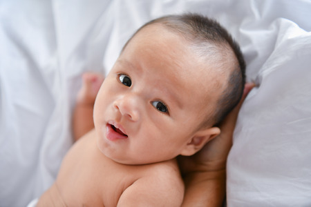 Newborn Concept. Mother and child on a white bed. Mom and baby boy playing in bedroom. Parent and little kid relaxing at home. Family having fun together. Newborn baby is fussing and crying.の写真素材