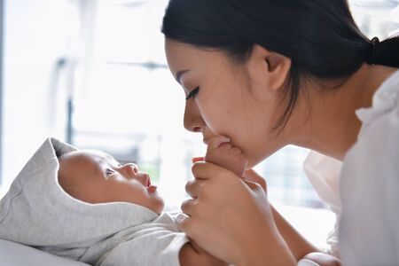 Newborn Concept. Mother and child on a white bed. Mom and baby boy playing in bedroom. Parent and little kid relaxing at home. Family having fun together. Newborn baby is fussing and crying.の写真素材