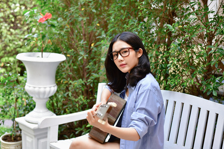 Music Concepts. Asian girls playing guitar. Asian women relaxing with music. Asian women have a happy lifestyle. Beautiful Asian girl playing guitar in the garden.の写真素材