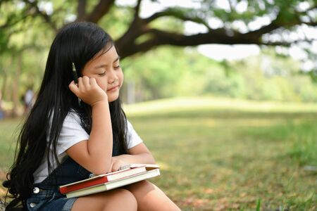 Education Concepts. The girl is reading a book in the garden. Beautiful girl is seriously studying. Beautiful girls are happy learning.の写真素材