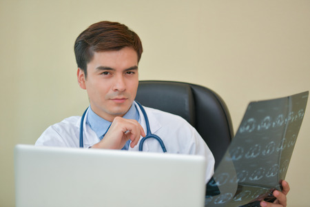 Smiling doctor posing in the office, he is wearing a stethoscope, medical staff on the hospital backgroundの写真素材
