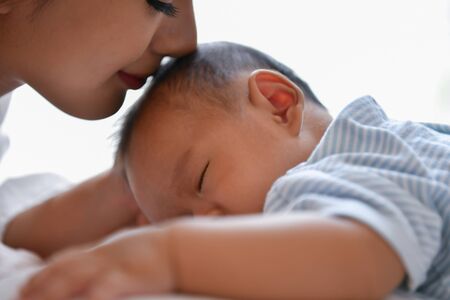 Newborn Concept. Mother and child on a white bed. Mom and baby boy playing in bedroom. Parent and...