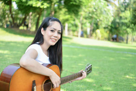 Music Concepts. Asian girls playing guitar. Asian women relaxing with music. Asian women have a happy lifestyle. Beautiful Asian girl playing guitar in the garden.の写真素材