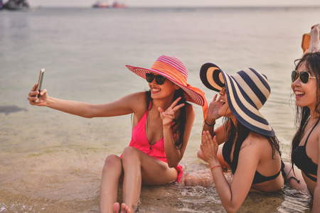 Swimsuit Concept. Beautiful girl wearing a swimsuit playing mobile on the beach. Beautiful girl is traveling on the beach. Beautiful girls are happy.の写真素材
