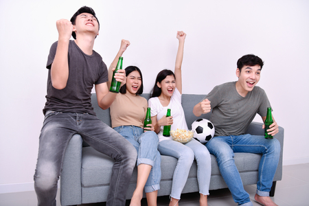Concept of cheering. Asian teenagers watching football on television. People are cheering and winning football scores.の写真素材