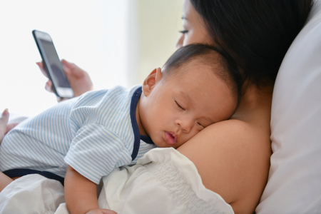 Newborn Concept. Mother and child on a white bed. Mom and baby boy playing in bedroom. Mother is...