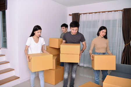 Moving house Concept. Asian young man is carrying his belongings. Young Asian women are holding...