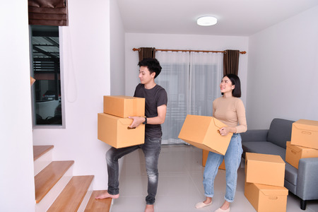 Moving house Concept. Asian young man is carrying his belongings. Young Asian women are holding their stuff in a paper box. Young are happy in the new house.の写真素材