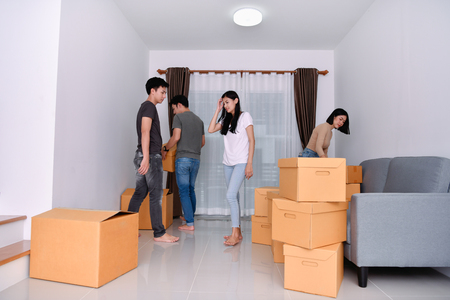 Moving house Concept. Asian young man is carrying his belongings. Young Asian women are holding their stuff in a paper box. Young are happy in the new house.の写真素材