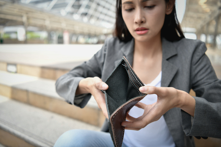 Concept of unemployed. Asian businesswoman is opening empty wallet. Young business woman is stressed because of no money.の写真素材