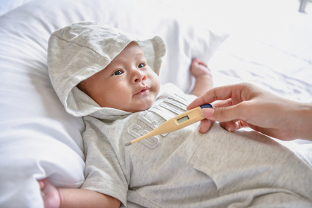 Newborn Concept. The baby is sick in the bedroom. Parents check their illness with thermometers.の写真素材