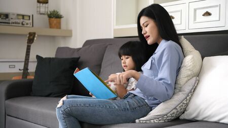 Family concept. Mother and daughter are reading books together in the living room.の写真素材