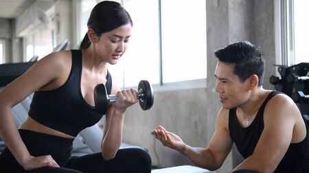 Exercise concept. The trainer is teaching women to raise dumbbells in the gym.の写真素材