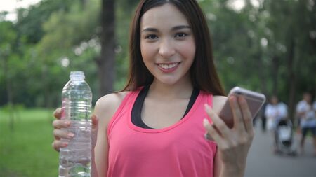 Exercise concepts. Young athletes are drinking and playing mobile in the park. 4k Resolution.の写真素材