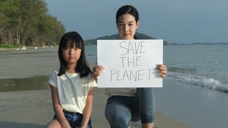 Campaign concept. The girl is carrying a banner for loving the world with a serious face on the beach. 4k Resolution.の写真素材