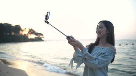 Holiday concept. Beautiful girl calling video on mobile to the beach. 4k Resolution.の写真素材