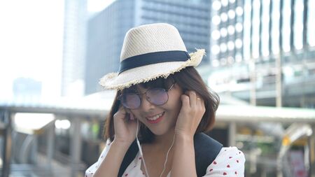 Travel concept. Beautiful women wearing headphones to listen to music in the business district. 4k...