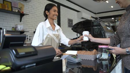 Coffee shop concept. The customer is accepting coffee and paying with a mobile phoneの写真素材
