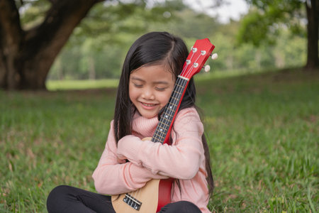 Asian girl hugging her ukulele in the garden. She loves playing music.の写真素材