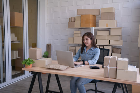 Asian woman checking online customer orders in office. She is using the computer for work.