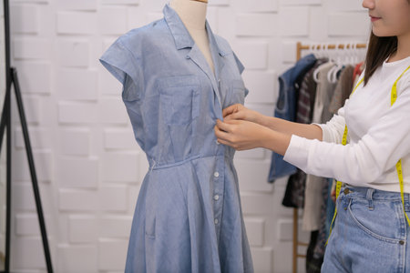 Asian tailor putting on a dress on a mannequin in a shop.
