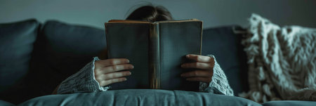 Selective focus of A woman lies on a sofa with a book covering his face in the living room.の素材