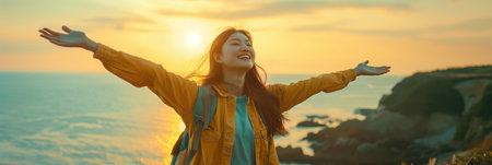 A smiling woman with a backpack is standing on a hill overlooking the ocean. her arms outstretchedの素材