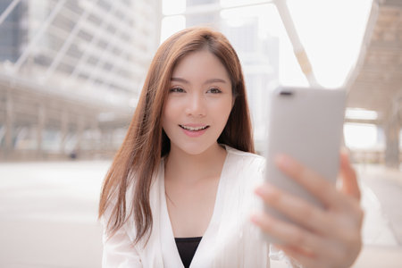 A young woman smiling while taking a selfie in an urban setting.の写真素材