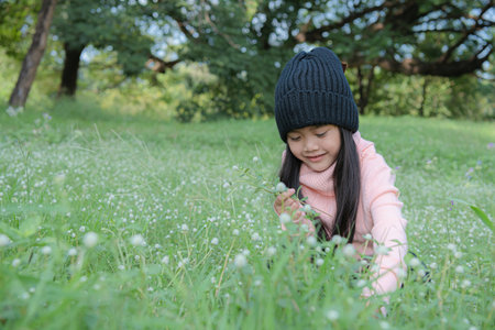 A young girl joyfully exploring wildflowers in a sunny green meadow.の写真素材