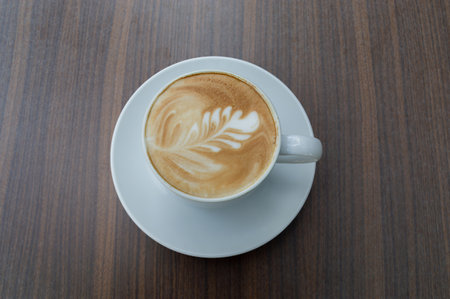 A beautifully crafted latte art in a white cup, resting on a wooden table, perfect for coffee enthusiasts.の写真素材