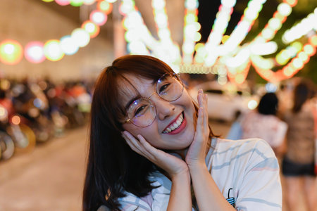 A cheerful young woman smiles widely, enjoying a festive atmosphere with vibrant lights in the background.の写真素材