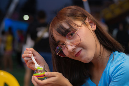 A young woman enjoys a colorful dessert, showcasing a playful and cheerful atmosphere with friends around her.の写真素材