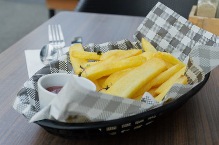 Delicious golden fries served in a stylish basket with a side of ketchup for dipping.の写真素材