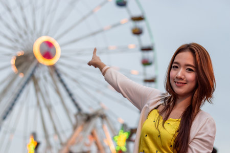 A joyful young woman pointing at a colorful ferris wheel, capturing the fun atmosphere of a carnival night.の写真素材