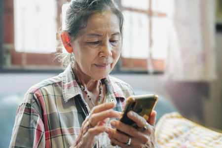 An elderly woman engages with her smartphone, highlighting technology&#39;s role in modern daily life.の写真素材