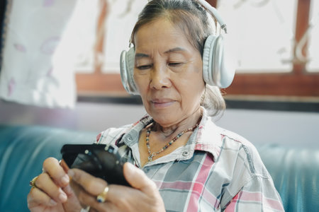 An elderly woman wears headphones while enjoying music on her smartphone, highlighting technology&#39;s impact on daily life.の写真素材